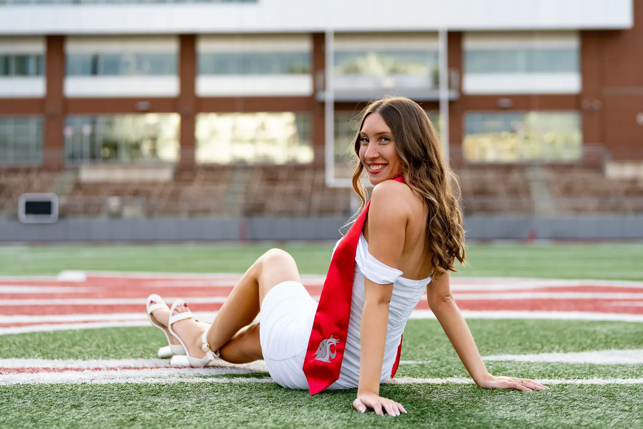 Graduate in a white dress and red stole lying back on the football field